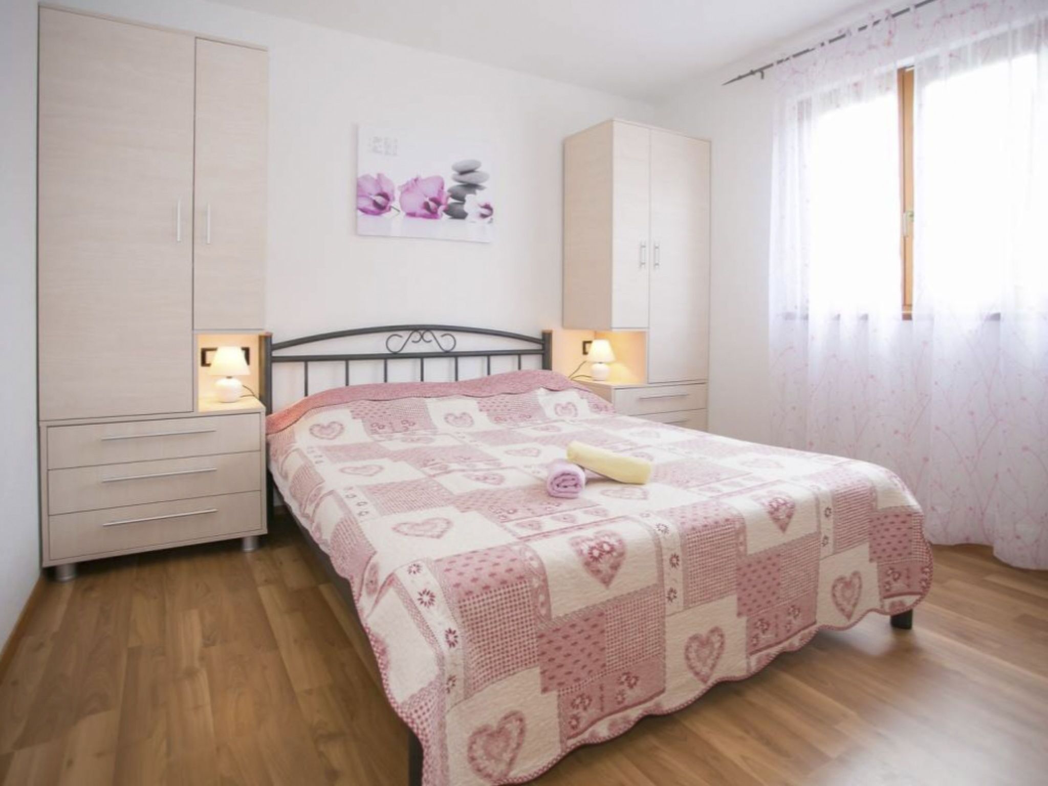 Un dormitorio con una cama, dos mesitas de noche, un armario y una ventana con cortinas.
