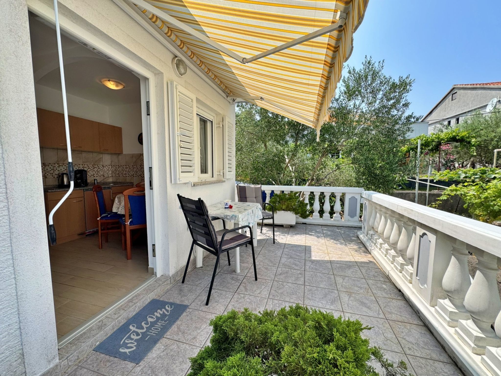 Un espace extérieur abrité, aménagé avec une table et des chaises, un paillasson et offrant une vue sur la verdure environnante.