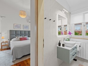 A modern bedroom with a large bed, bedside table, and a hanging light fixture. The bathroom features a white sink, mirror, and window with a view of the outside. - Villa Mia Lea für 6 Personen by Interhome (Poreč/Tar)