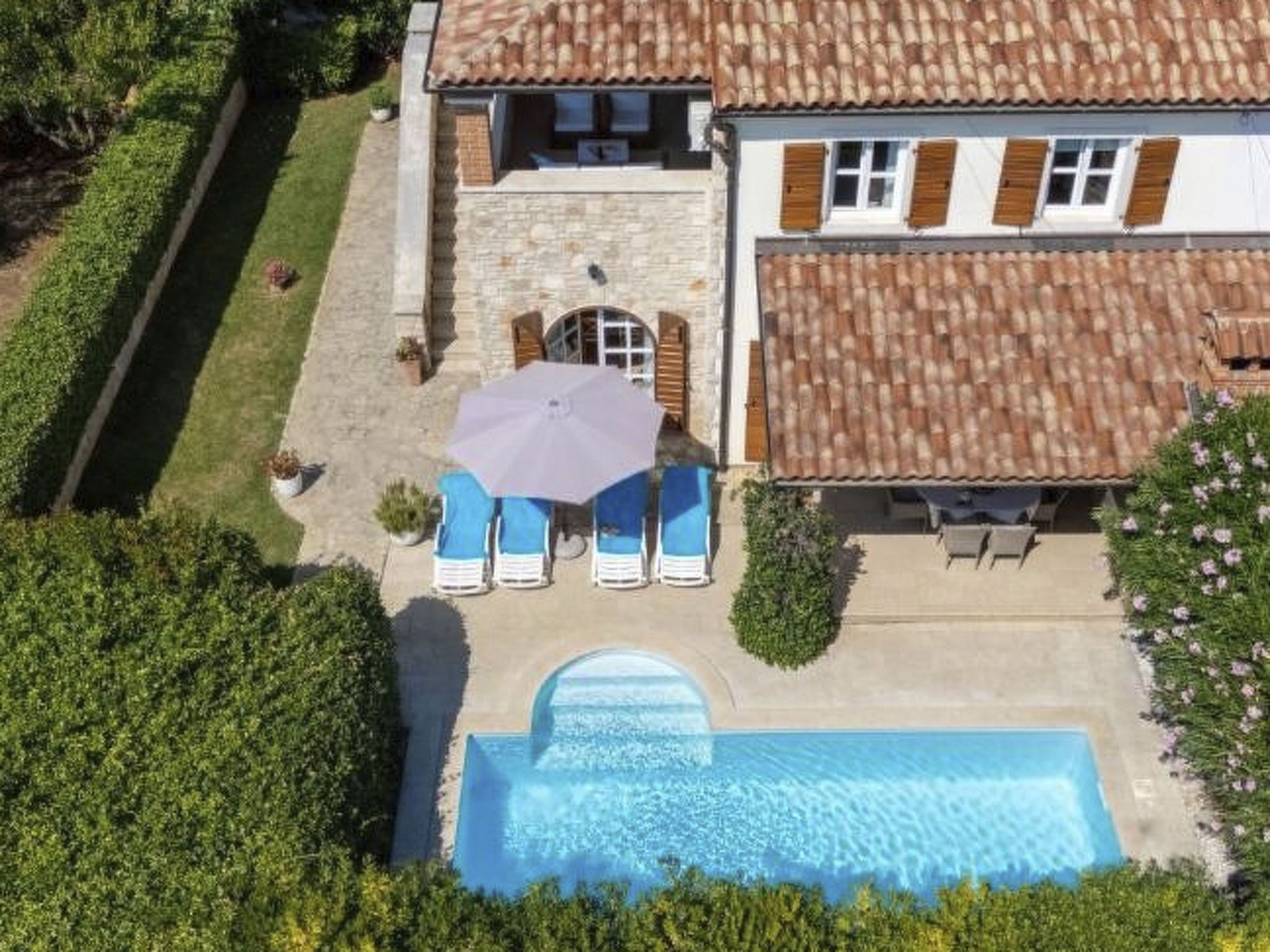 Uma casa de dois andares com piscina, um pátio com cadeiras de descanso e um jardim.