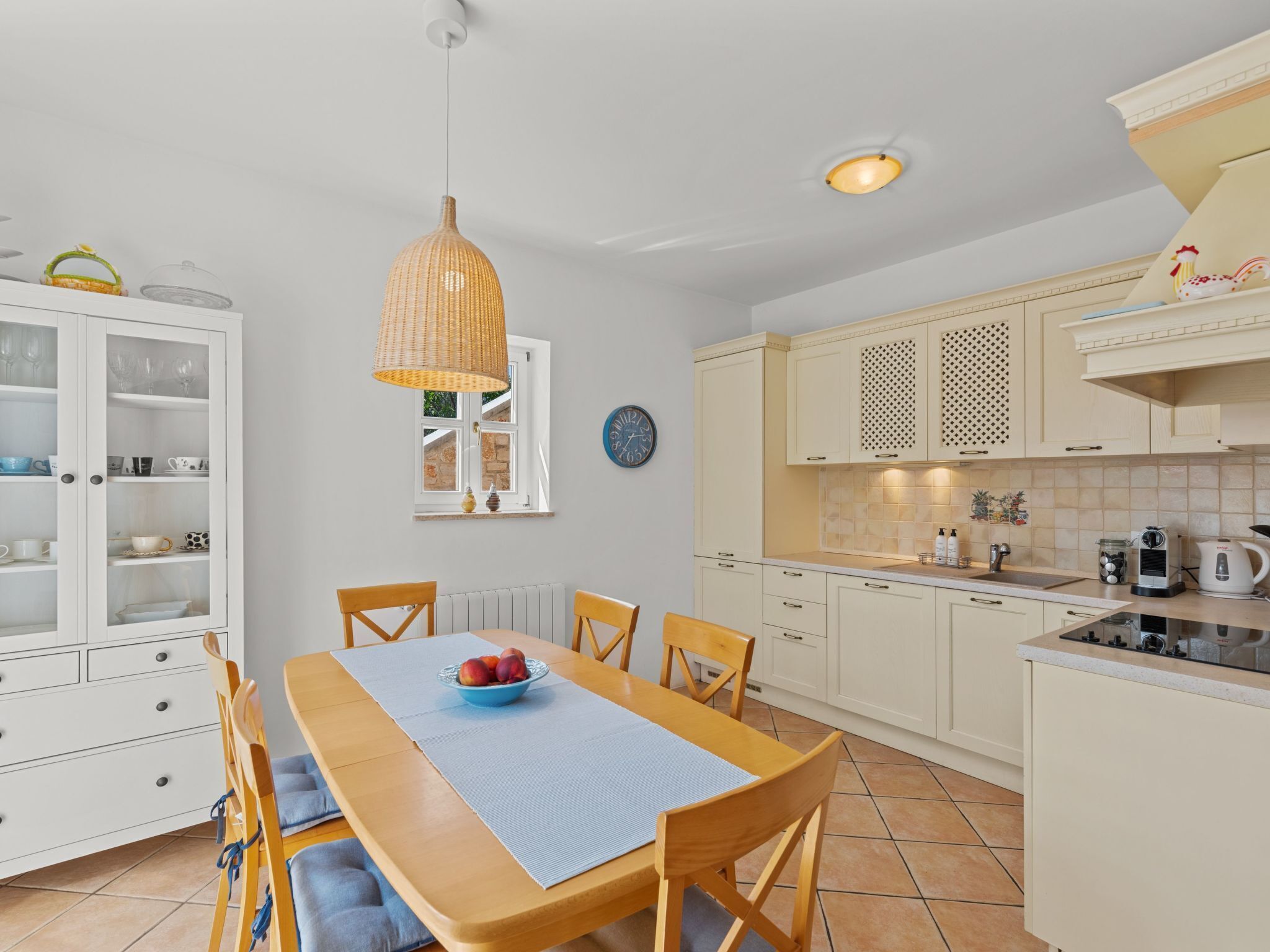 A compact kitchen with white cabinets, a dining table with blue cushions, and a wicker pendant light.