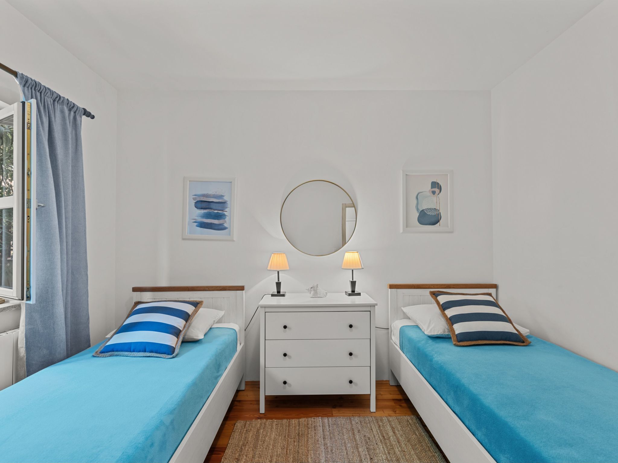 Quarto com duas camas de solteiro, mesa de cabeceira com luminárias, espelho e obras de arte nas paredes.