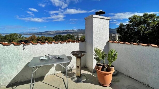 Terraza en la azotea con mesa, parrilla y plantas en macetas.