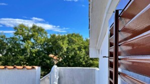 Un estrecho pasillo exterior con una pared blanca y una puerta marrón.