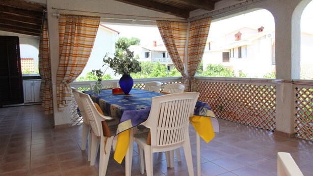 A covered outdoor dining area with a table set for four, surrounded by white chairs, and a blue tablecloth. - Apartment Andjela by Interhome (Krk/Šilo)