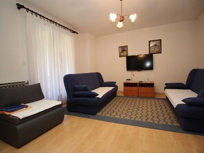 Ein modernes Wohnzimmer mit zwei dunkelblauen Sofas, einem Holztisch, einem Flachbildfernseher und einem gemusterten Teppich.