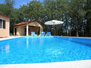 En pool med två solstolar och en möblerad sittplats under tak.