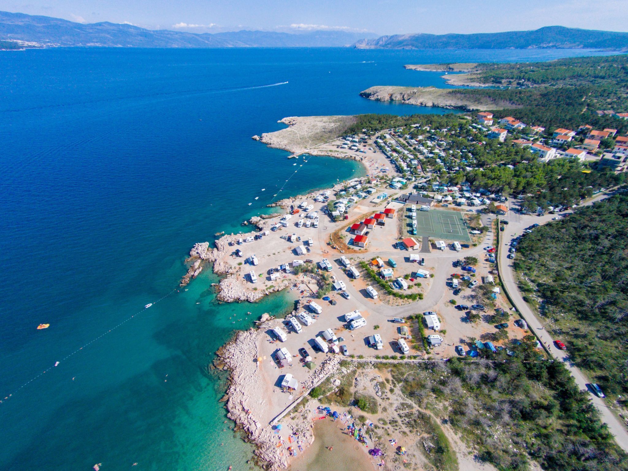 Luftaufnahme einer Küstenregion mit Strand, Stellplätzen für Wohnmobile und einem Tennisplatz.