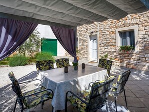 Eine Terrasse im Freien mit einem runden Tisch und Stühlen, ein Steinhaus mit einer grünen Tür und Topfpflanzen.