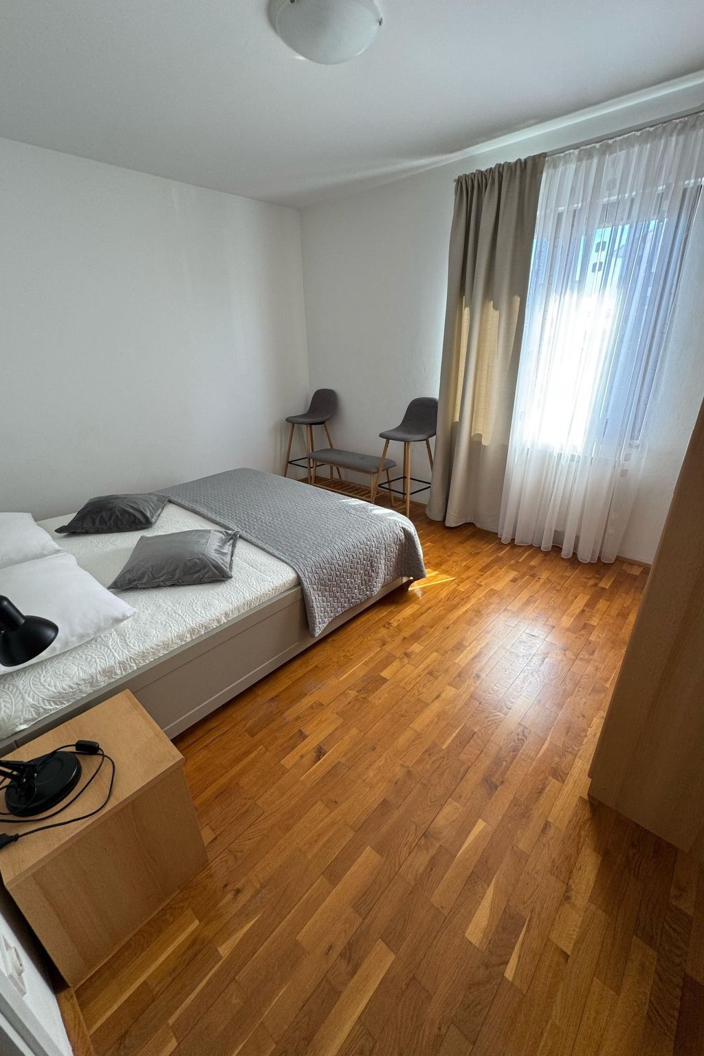 A bedroom with a bed, two chairs, a desk with a computer, and a window with curtains.