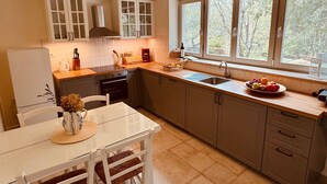 Una cocina moderna con armarios blancos, encimera de madera, una mesa de comedor con sillas y un ventanal con vistas a árboles.