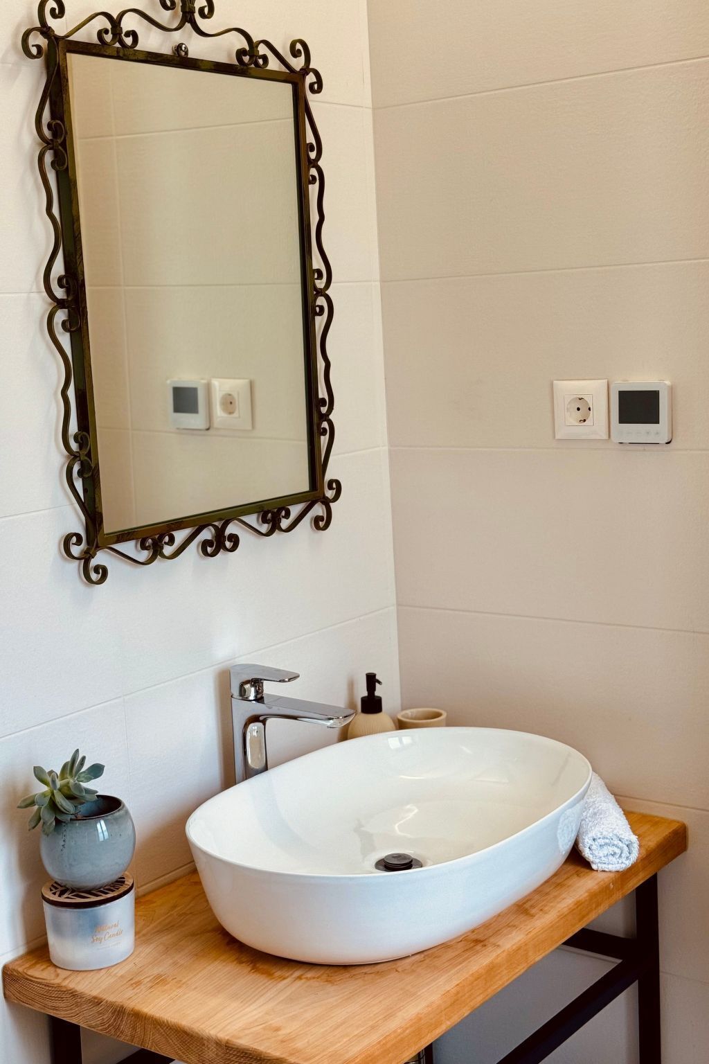 Une salle de bain avec un lavabo blanc, un miroir doté d’un cadre orné, une serviette et une petite plante.