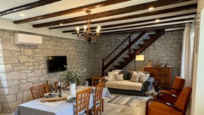 Un comedor con pared de piedra, vigas de madera, una araña y un sofá al fondo.