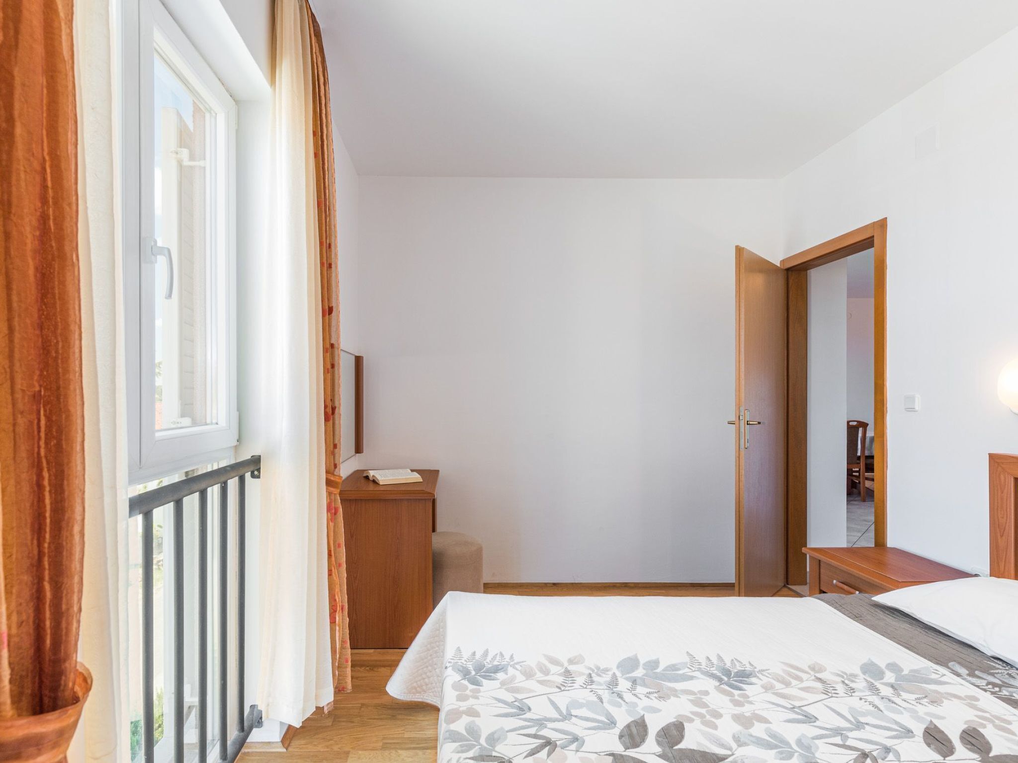 Un dormitorio con una cama, una mesita de noche de madera, un espejo y una ventana con cortinas.