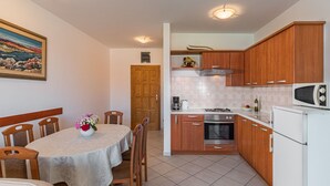 Una cucina compatta con mobili in legno, un forno a microonde, un piano cottura e un lavandino. C'è un tavolo da pranzo con sedie e un vaso di fiori.