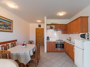 A compact kitchen with wooden cabinets, a microwave, a stove, and a sink. There is a dining table with chairs and a vase of flowers. - Pinta mit großem Garten by Interhome (Buzinija)