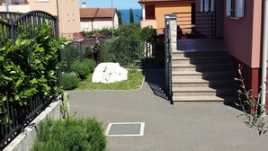 Un vialetto lastricato conduce a un edificio con tetto in tegole rosse e un muro in pietra.