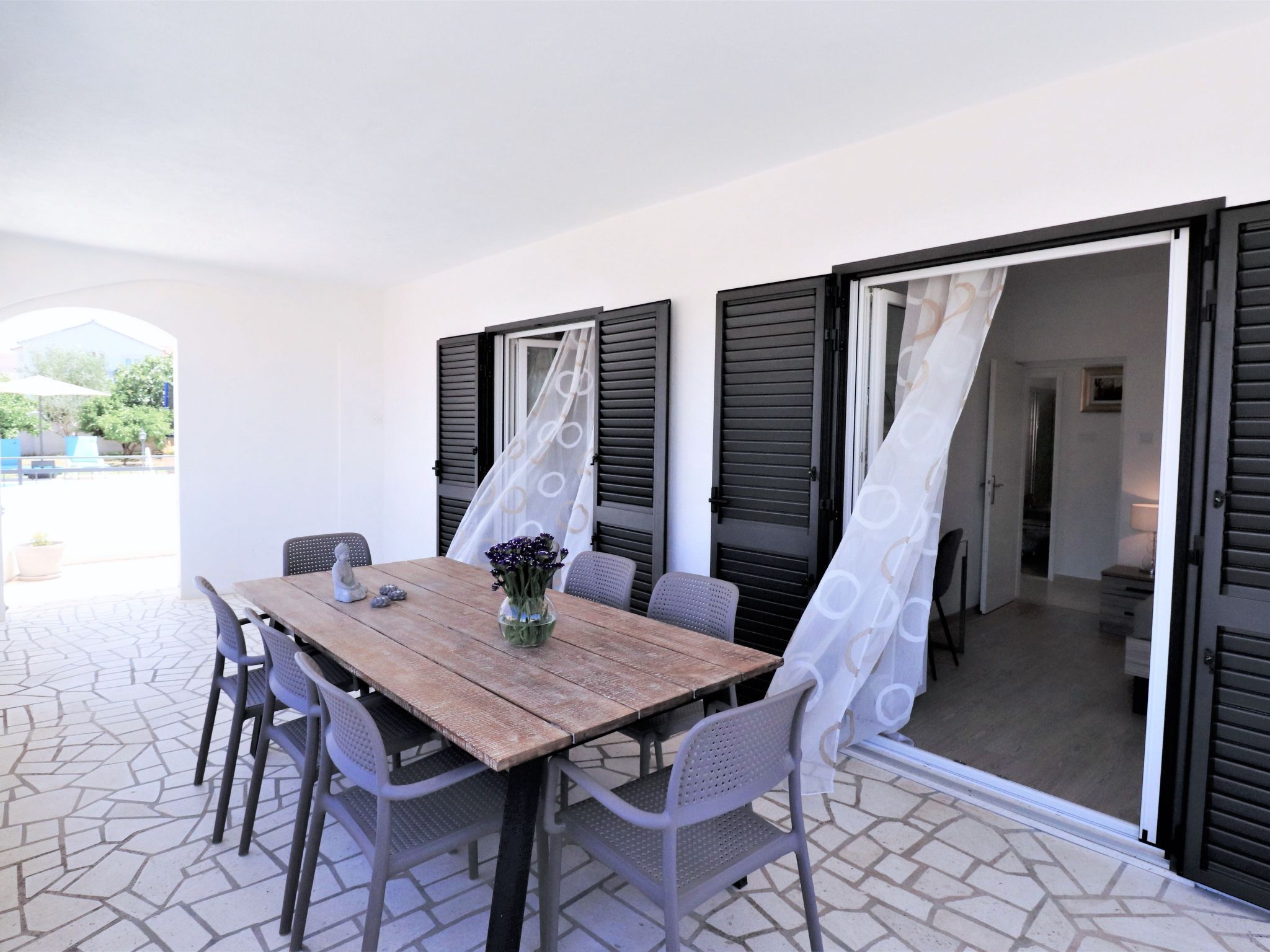 Un patio con una mesa y sillas de madera, un jarrón con flores y una vista a través de una puerta.