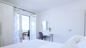 Una camera d'albergo con un letto, una scrivania, una sedia, uno specchio rotondo e vista sull'esterno.