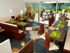 A modern dining area with multiple tables and chairs, a glass partition, and a view of the outdoors. - Hartlbauer in Dorfgastein by Interhome (Dorfgastein)