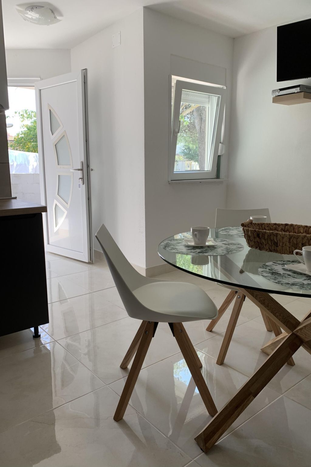 A modern dining area with a glass table, white chairs, and a wicker basket.