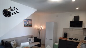 Una cocina moderna con refrigerador, estufa y microondas. Hay una mesa de comedor con sillas y una mesa de centro de vidrio. También se ve un sofá y un reloj decorativo en la pared.