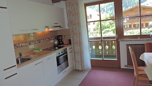 A kitchen with white cabinets, a stainless steel sink, a coffee maker, and a window with a view of buildings and trees. - in Dorfgastein by Interhome (Dorfgastein)