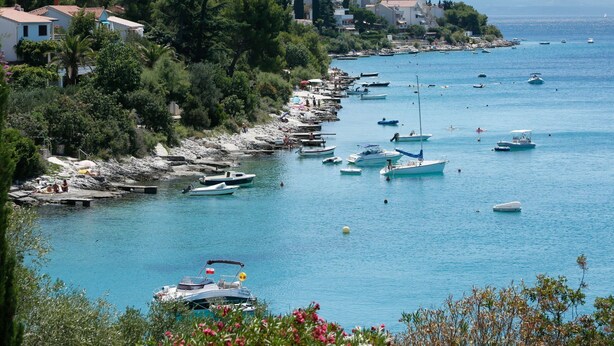 Uma cidade costeira com barcos atracados na orla, uma praia rochosa e edifícios ao fundo.