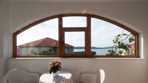 A room with a large arched window, a small round table with a floral tablecloth, two white chairs, and a vase with flowers. - Wohnung mit Blick auf das Wasser by Interhome (Trogir)