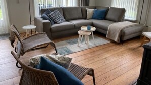 Un salón con un sofá seccional gris, dos sillones de mimbre, una mesita redonda y una mesa de centro.