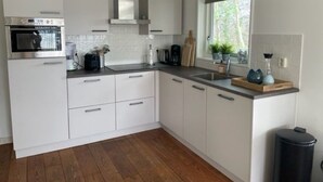 Una cocina moderna con armarios blancos, horno empotrado, ventana con vistas y un cubo de basura negro.