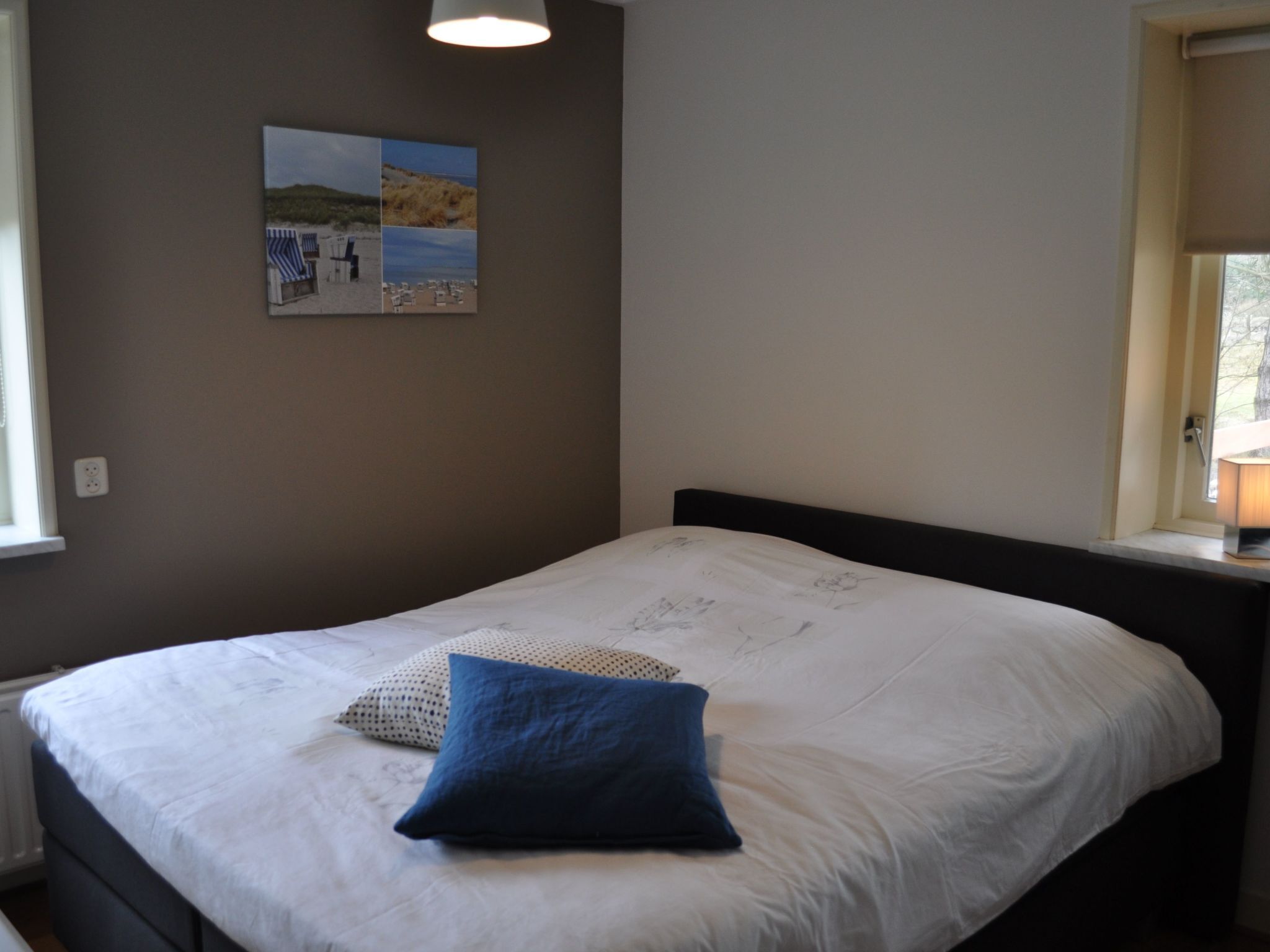 Une chambre avec un lit simple, une lampe fixée au mur et une fenêtre donnant sur des arbres.