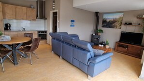 Un salon moderne avec un canapé bleu, un coin repas avec une table et des chaises en bois, une cuisine avec des meubles en bois, une cheminée et un téléviseur.