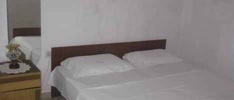 Een eenvoudige, nette kamer met een enkel bed, een houten nachtkastje en een bijzettafeltje met een lamp.