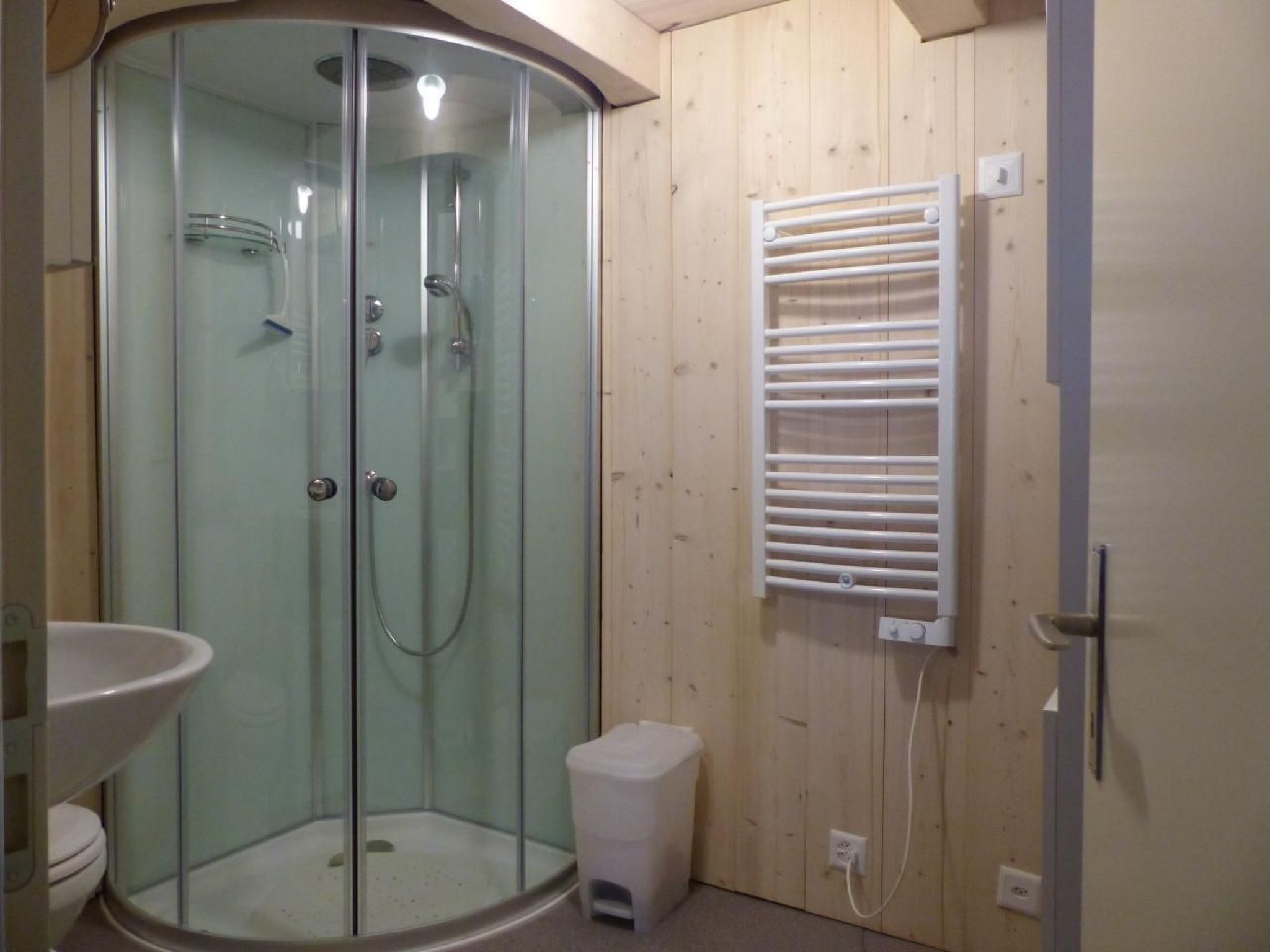 A small, enclosed shower area with a glass door, a white sink, and a towel rack on the wall.