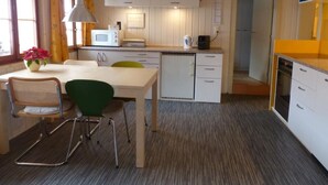 A compact kitchen with white cabinets, a microwave, and a coffee maker. There is a dining area with a table and chairs, and a small refrigerator.