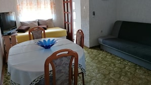 Une petite pièce agréable et chaleureuse, avec une table à manger, des chaises, un canapé, un téléviseur et une fenêtre avec des rideaux.