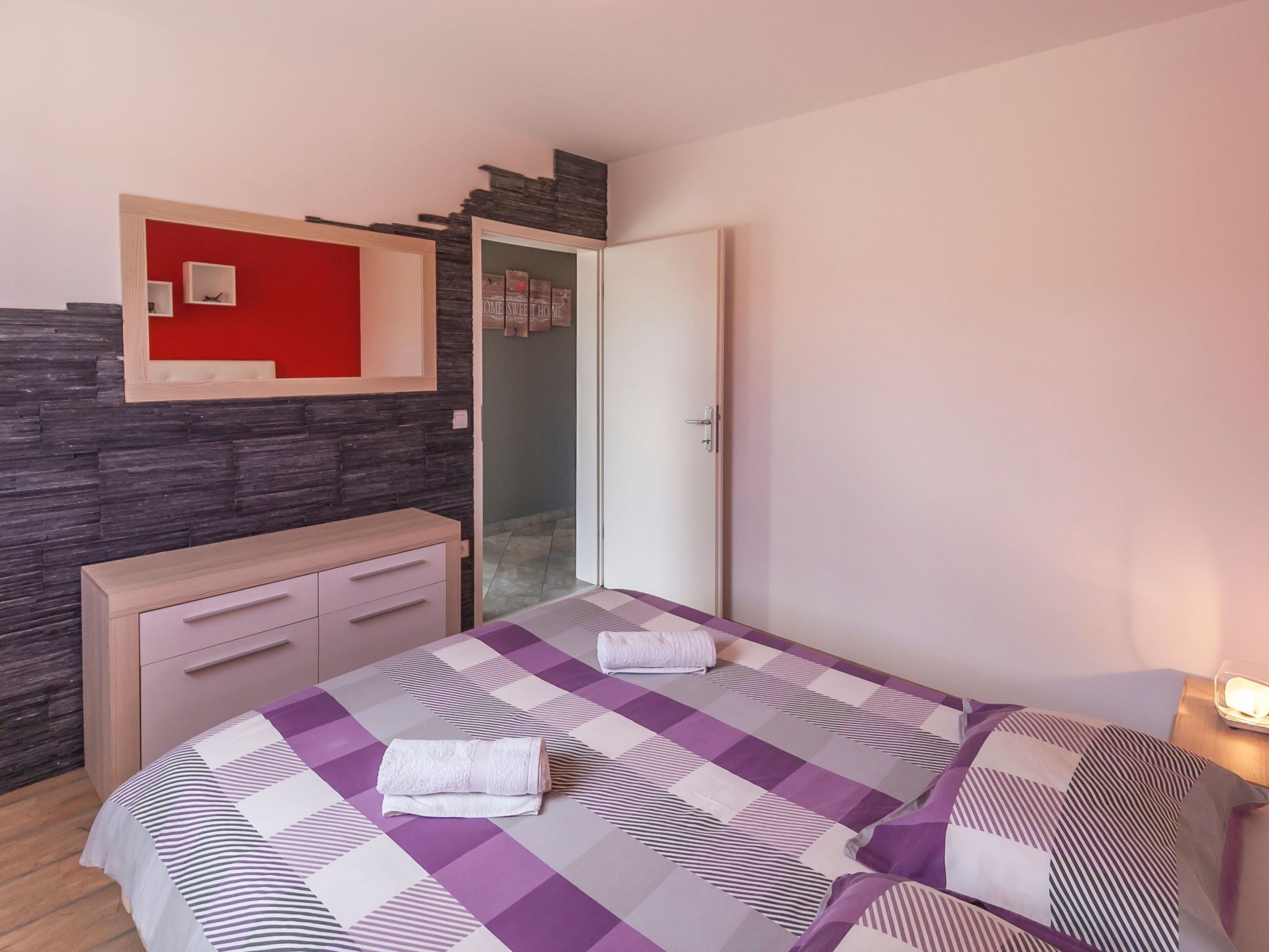 Une chambre à coucher avec un lit, une commode, un miroir et un mur d’accent de couleur rouge.