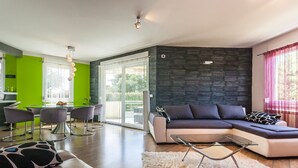 En moderne stue med en hjørnesofa, et spiseområde med et glasbord, og et køkken i baggrunden.