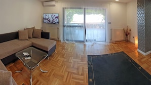 Un salon moderne avec un canapé, une table basse en verre et une porte-fenêtre coulissante donnant sur un espace extérieur.