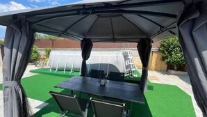 Un patio cubierto con una mesa y sillas, rodeado de césped artificial verde.