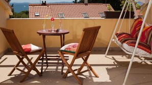 A balcony with two wooden chairs, a small round table with a vase and glasses, and a hanging swing with colorful cushions. - Ruhige Ferienwohnung mit herrlicher Aussicht by Interhome (Dragovode)