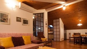 A cozy living room with a wooden ceiling, a pink sofa with yellow cushions, a dining table with chairs, and a kitchen visible through a glass door. - Ruhige Ferienwohnung mit herrlicher Aussicht by Interhome (Dragovode)