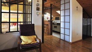 A spacious room with a large window, wooden flooring, a chair with a cushion, and a kitchen area visible through a sliding door. - Ruhige Ferienwohnung mit herrlicher Aussicht by Interhome (Dragovode)