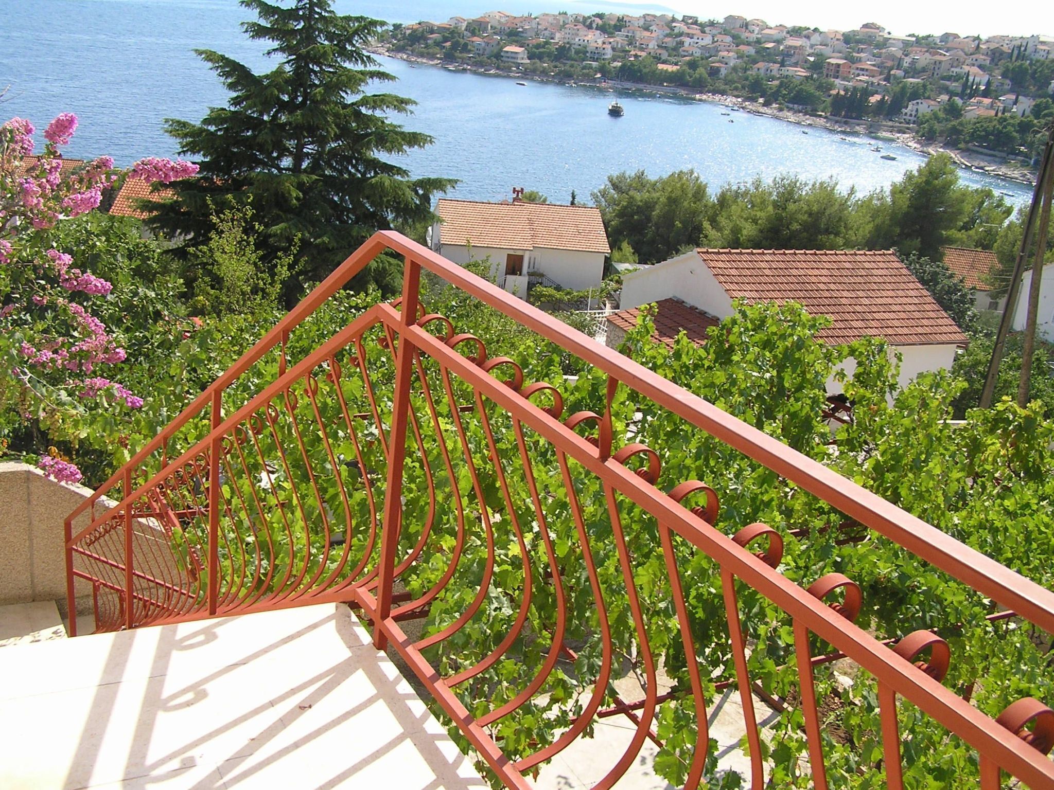 A balcony with a red railing overlooking a coastal town.