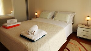 Een net opgemaakt bed met gevouwen handdoeken, een bedlamp en een klein nachtkastje.
