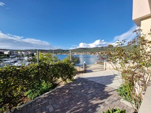 A paved pathway leading to a marina with boats, a clear blue sky, and distant hills. - mit zwei Balkonen by Interhome (Vinišće)