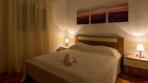 A neatly made bed with a rolled towel, two bedside lamps, and three landscape paintings on the wall. - Modernes Ferienhaus mit Terrasse und Meerblick by Interhome (Vinišće)