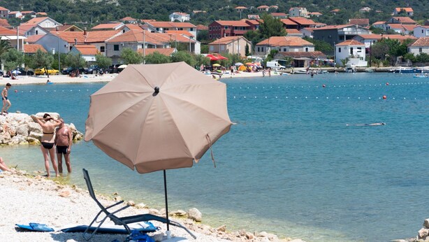 A beach with clear waters, a sandy shore, and a row of houses in the background. - Modernes Ferienhaus mit Terrasse und Meerblick by Interhome (Vinišće)