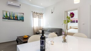 A modern living room with a white sofa, a dining table with a bottle of wine and glasses, a painting of sailboats, and a flower vase. - Modernes Ferienhaus mit Terrasse und Meerblick by Interhome (Vinišće)